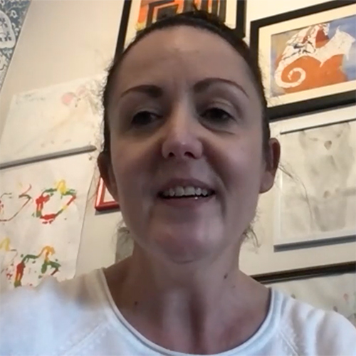 Woman smiling with pictures on a wall behind her